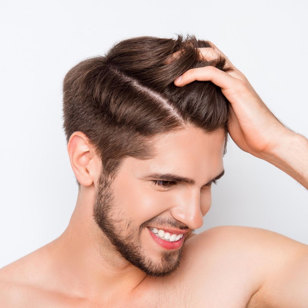 Young, clear-skin beareded man holding a luscious tuft of hair demonstrating hair regeneration by Dr Django Nathan at Medical Injectables in Wollongong and Orange NSW