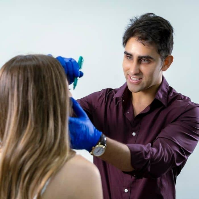 The handsome Dr Django Nathan marking cosmetic treatment injection points on a lovely young lady with long hair to the door of the consulting room t Medical Injecatbles in Wollongong and Orange, NSW